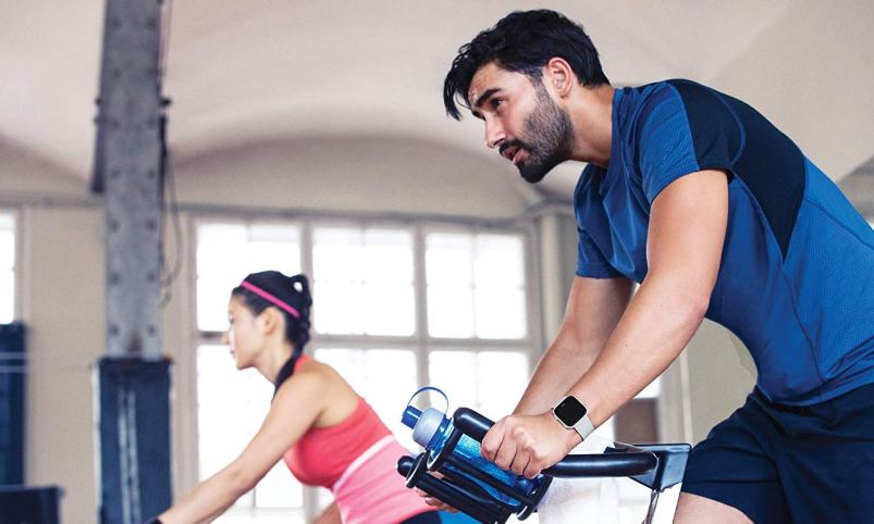 Mann und Frau mit Fitbit Versa Smartwatch auf dem Ergometer Mann und Frau mit Fitbit Versa Smartwatch auf dem Ergometer