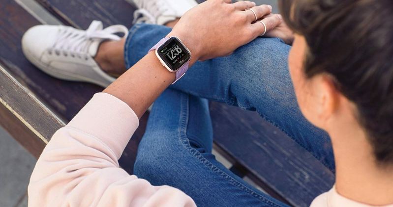 Frau schaut auf Fitbit Versa Smartwatch am Handgelenk Frau schaut auf Fitbit Versa Smartwatch am Handgelenk