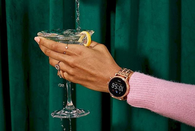 frau haelt glas mit fossil julianna hr smartwatch am handgelenk frau haelt glas mit fossil julianna hr smartwatch am handgelenk