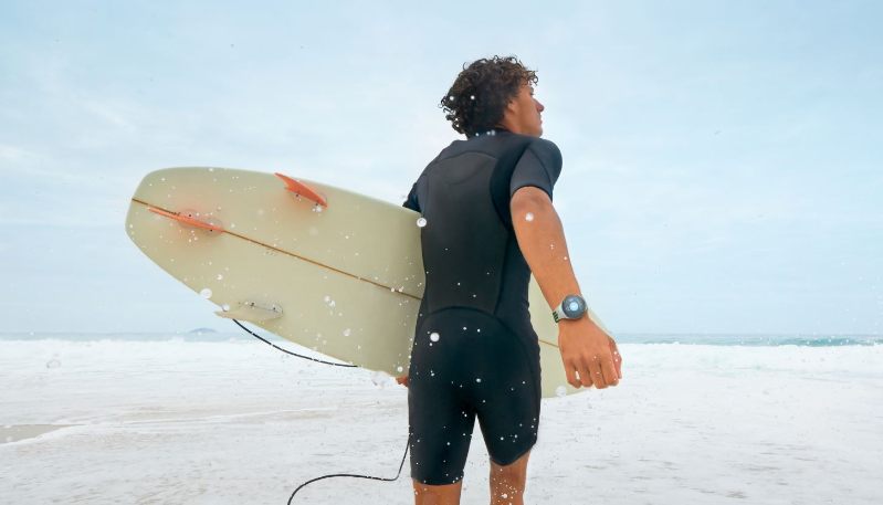 mann mit surfbrett am strand und huawei watch gt 2e hector am handgelenk
